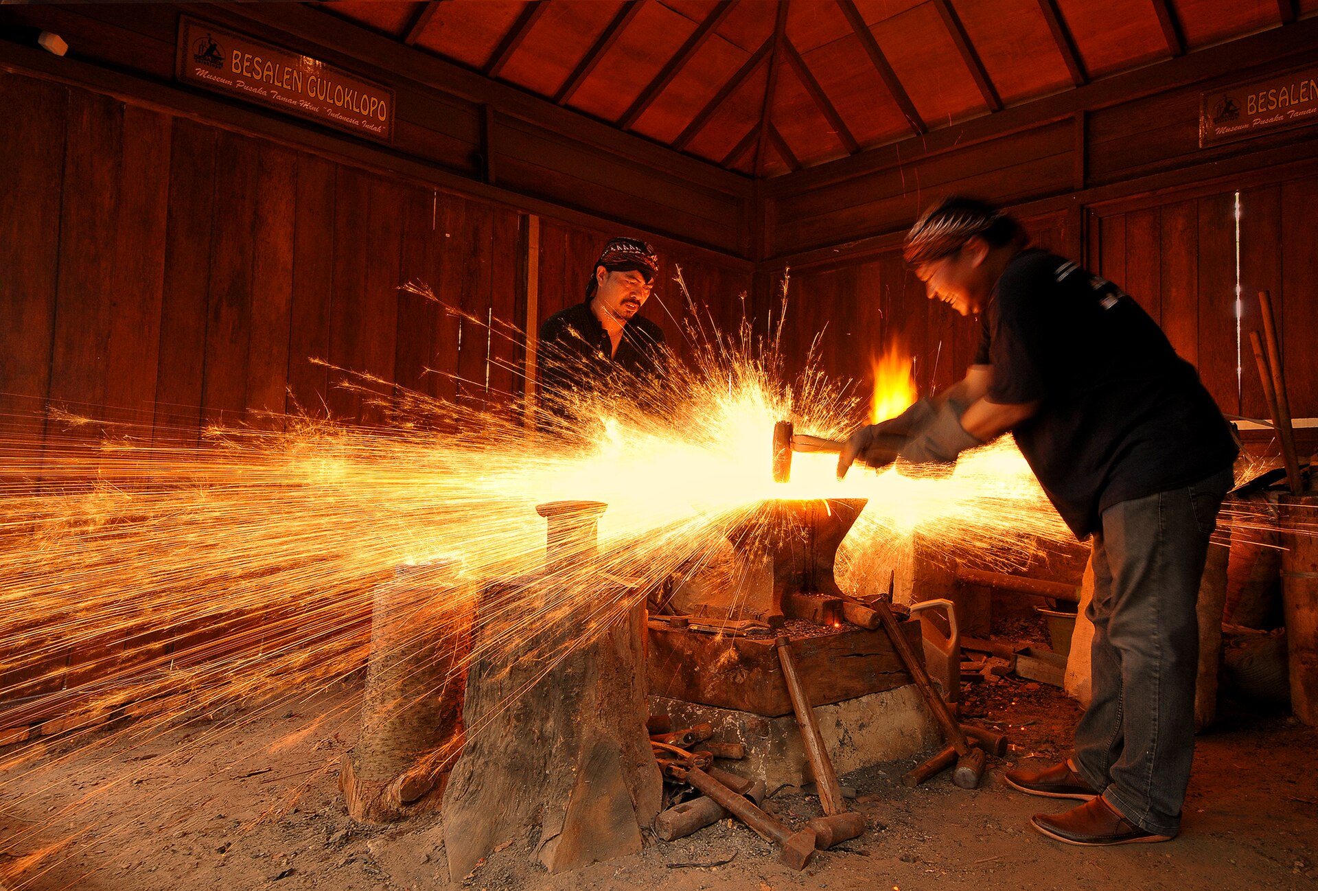 Кузнецы куют раскалённый металл у горна, в стороны летит сноп оранжевых искр